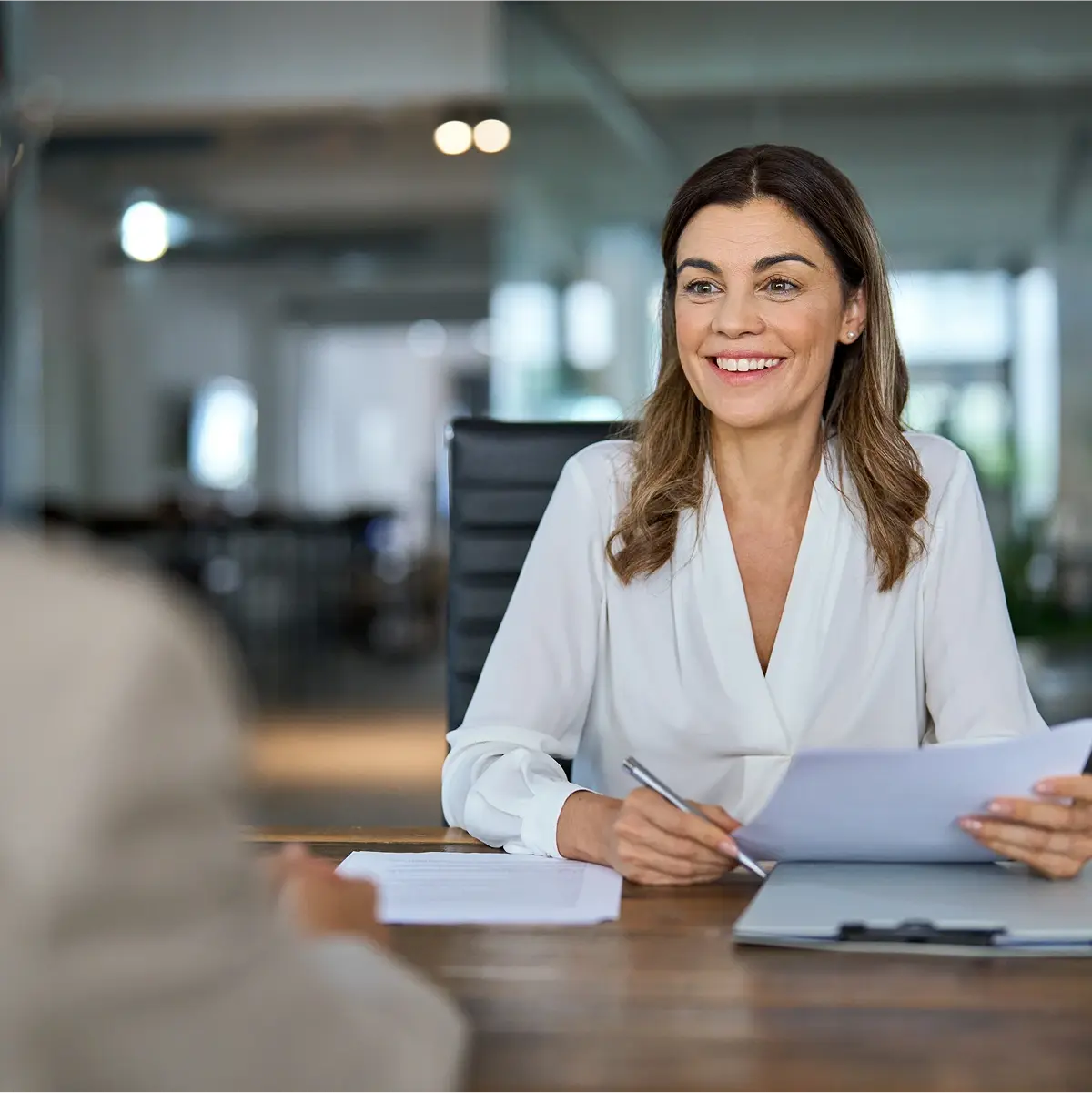Woman sitting at a wooden table interviewing another person.