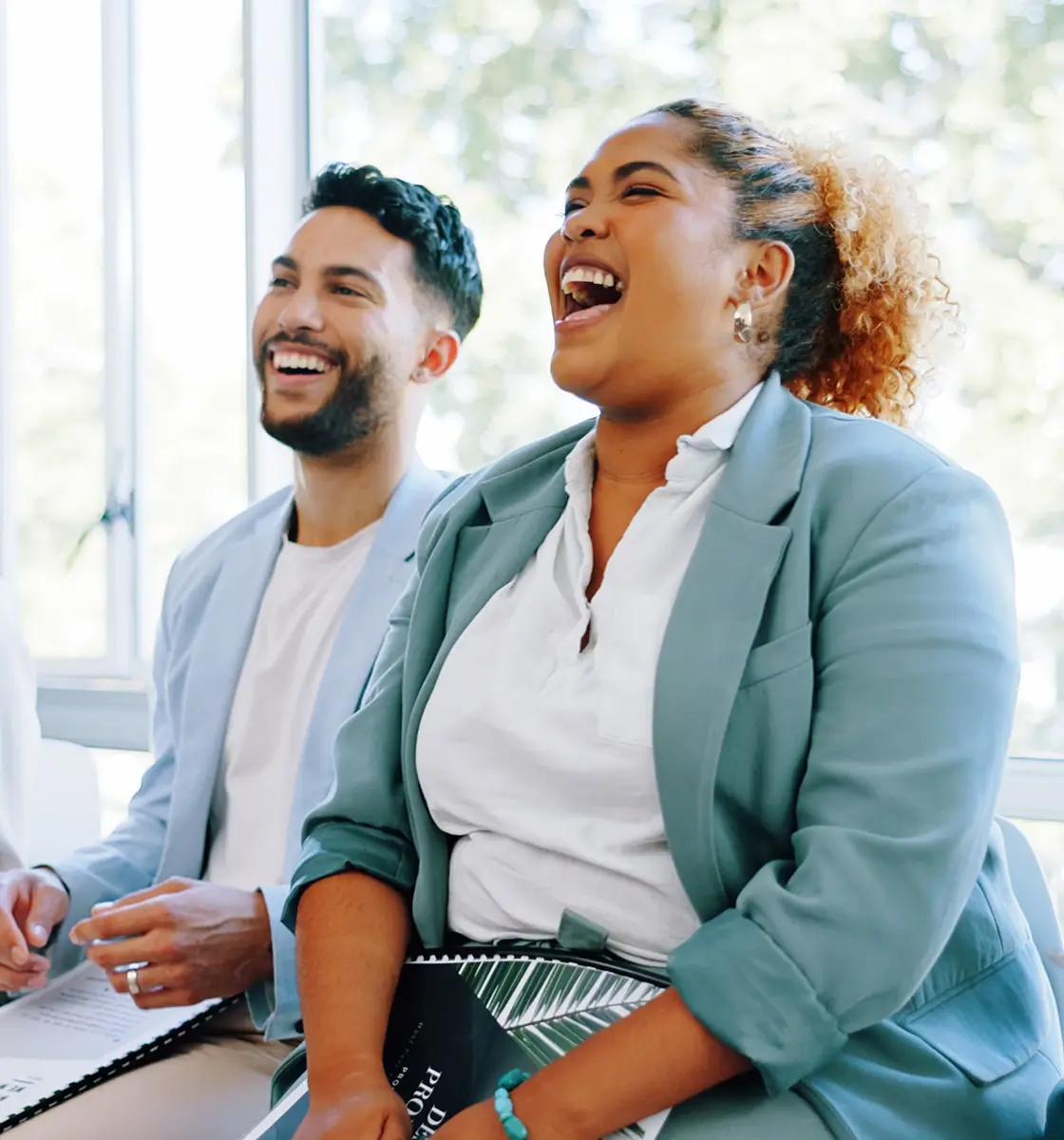 Two colleagues sit side by side engaging in laughter.