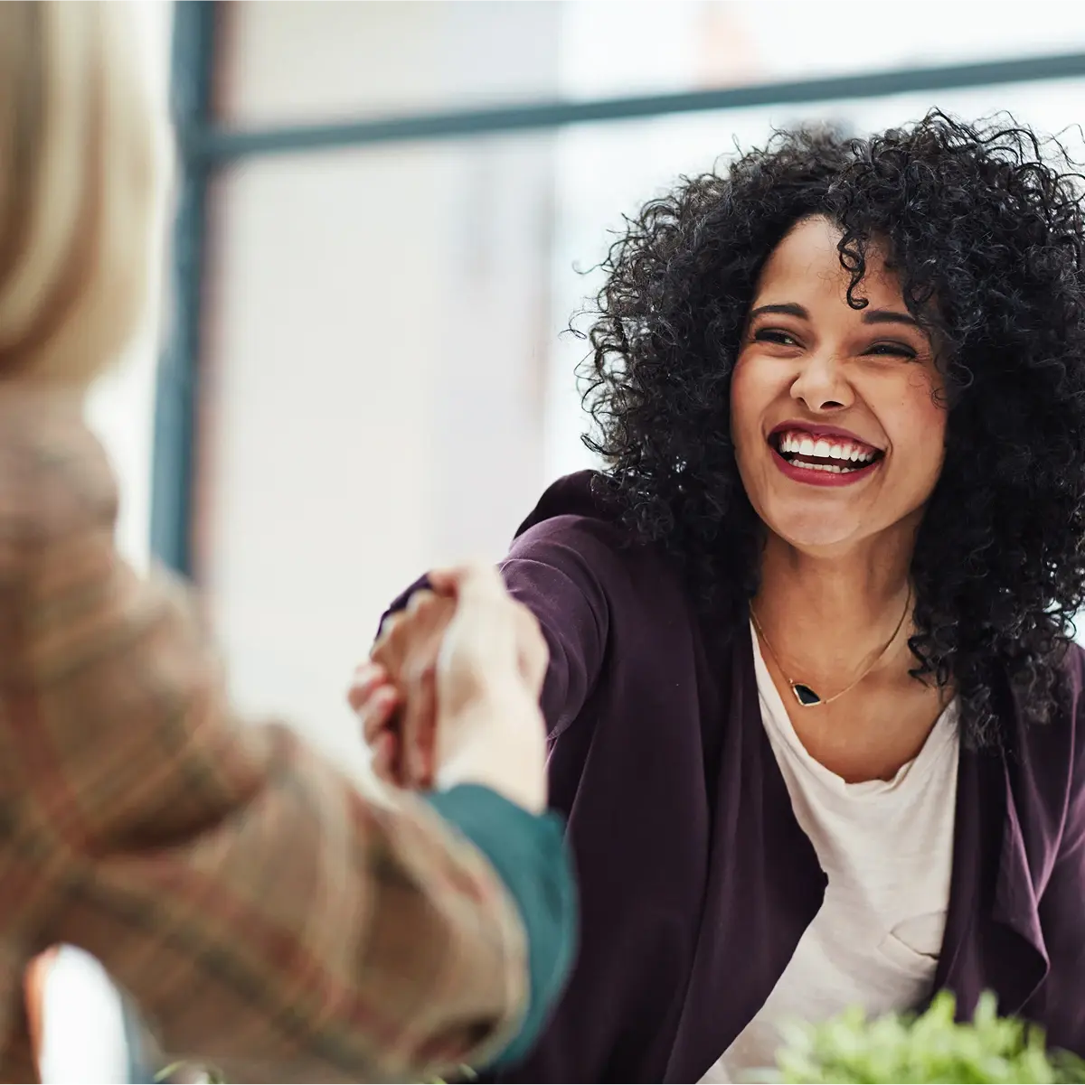 Woman wearing eggplant colored soft blazer shakes hand with another person.